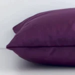 Velvet plum cushion laying on its side. The solid colour design and its square size are visible.