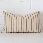 A brick wall that has a striped cushion cover positioned in front of it. It has an exquisite designer material and a lovely rectangle shape.