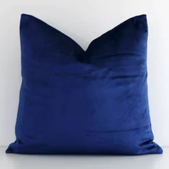 Velvet square cushion with a solid colour design in an upright position against a white white wall. It is royal blue in colour.