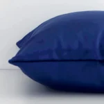 A sideways perspective of this solid-coloured velvet cushion. The positioning shows the border of the square shape and the royal blue colour.