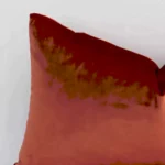 A rust velvet cushion cover’s corner is shown in more detail. It is possible to see the corner of a rectangular design and solid colour finish in much more detail.