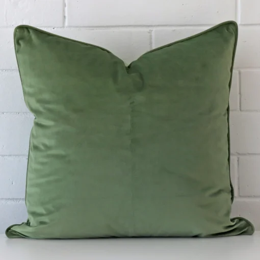 Sage cushion positioned in front of a brick wall. It has large dimensions and is made from a velvet material.
