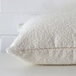 Horizontal edge view of front and back panels of a boucle cushion in a large size and with white colouring.