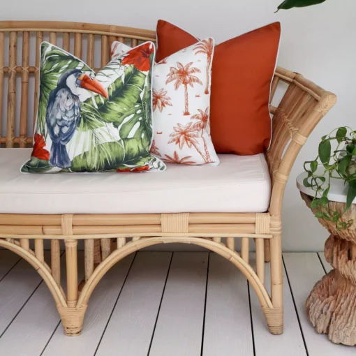 3 terracotta outdoor couch cushions including one with a toucan and a palm tree design.