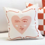 Tropica cushion with pink heart face design and red border details.