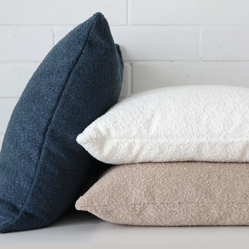 A white wall has a stack of boucle cushions placed in front of it.